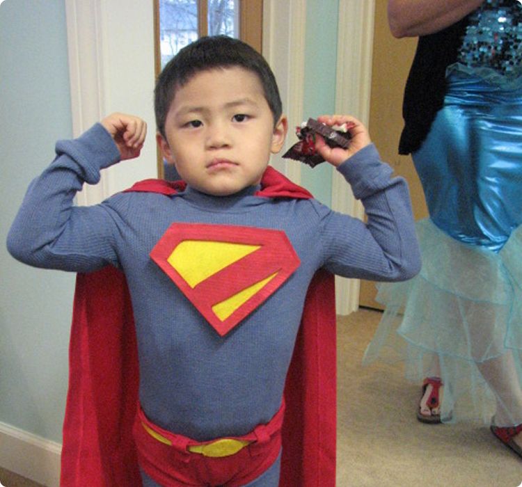 First visit page content image 2 Young boy in superhero costume flexes arms, posing confidently at a party.