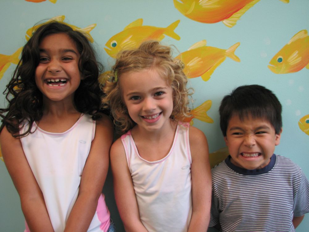 Service page content image 2 Three kids standing against a wall with fishes on it smiling and making funny faces