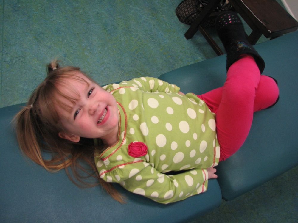 Young girl smiling and lying on dental chair, showing comfort and positivity during visit.