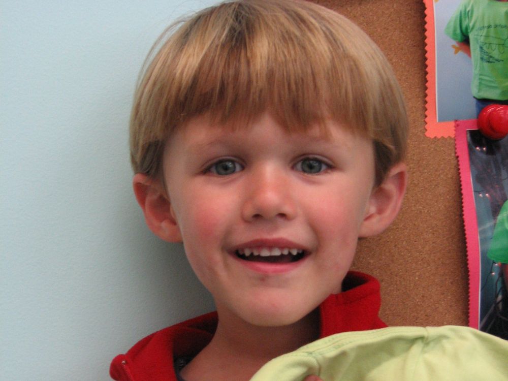 Smiling young boy with bright eyes, showing happiness and comfort in a friendly setting.