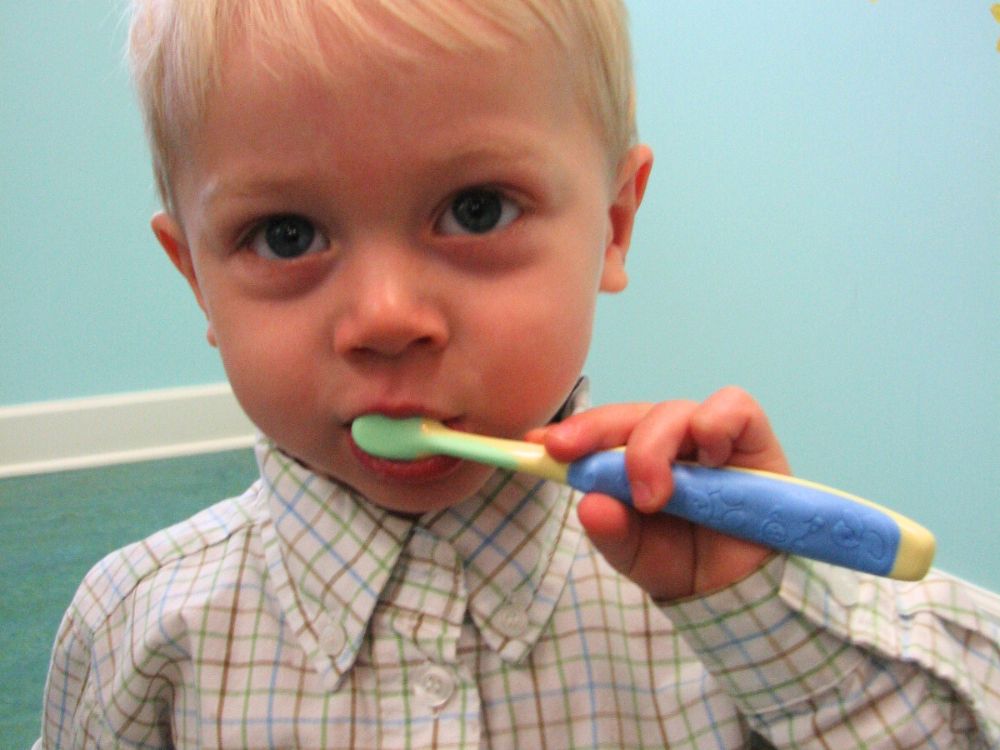 A young child wearing a button-up shirt brushing their teeth