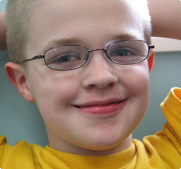 Testimonials page content image 1 Close-up of smiling boy wearing glasses, showing friendly expression in a dental setting.