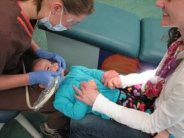 Updated service page image stack photo 1 Dental professional treating young child while parent holds child’s hand, showing supportive pediatric dental care.