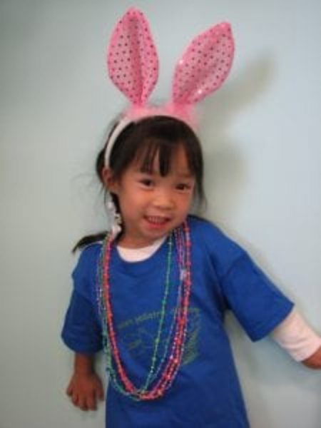 Updated service page image stack photo 2 Young girl wearing pink bunny ears and colorful beads smiles, showing playful fun in a welcoming setting.