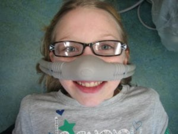 Updated service page image stack photo 5 Girl wearing glasses and a dental nose mask smiles while lying back in dental chair, showing comfort during treatment.