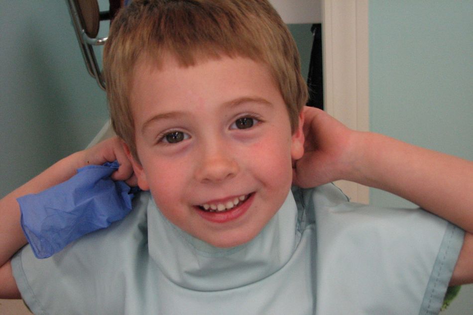 A young boy sitting in the dental exam chair smiling