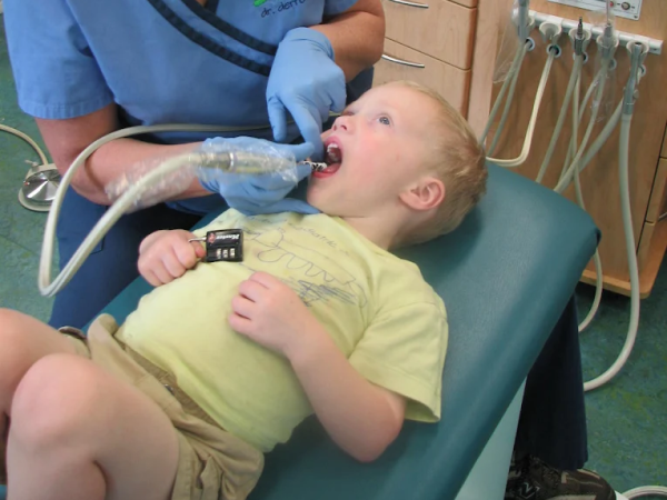 service page image stack photo 3 Dental professional cleaning young boy’s teeth while he lies calmly in dental chair, showing supportive pediatric care.