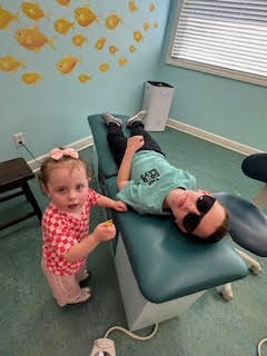 A little girl standing beside a patient in the chair